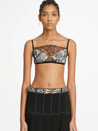 Portrait of a woman wearing a lace bra top, black skirt with white stitching, and patterned belt on a white backdrop.