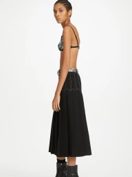 Model in black pleated skirt and patterned top standing against a plain white background for Dion Lee.