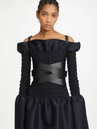 Model wearing a black off-the-shoulder dress with structured leather harness by Dion Lee against white background