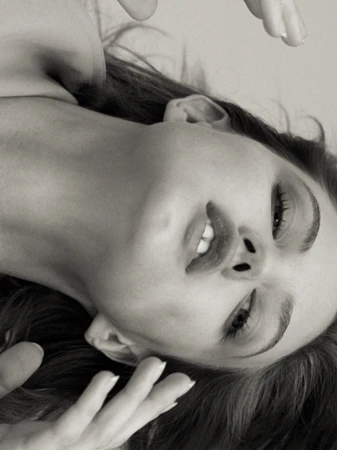 Monochrome portrait of a smiling woman with hands near her face, close-up, in a studio with diffused light, capturing a beauty moment.