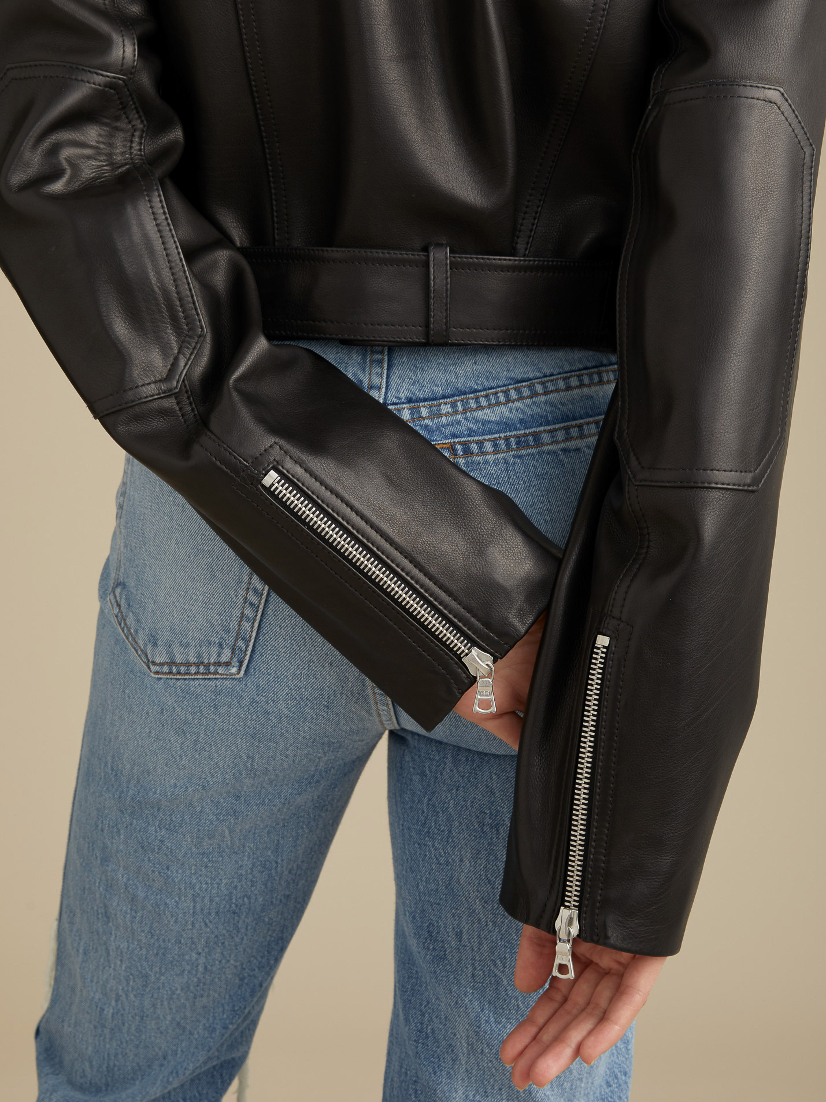 Close-up shot of a person in light wash jeans and a black leather jacket with silver zippers, showcasing fashion and style details.