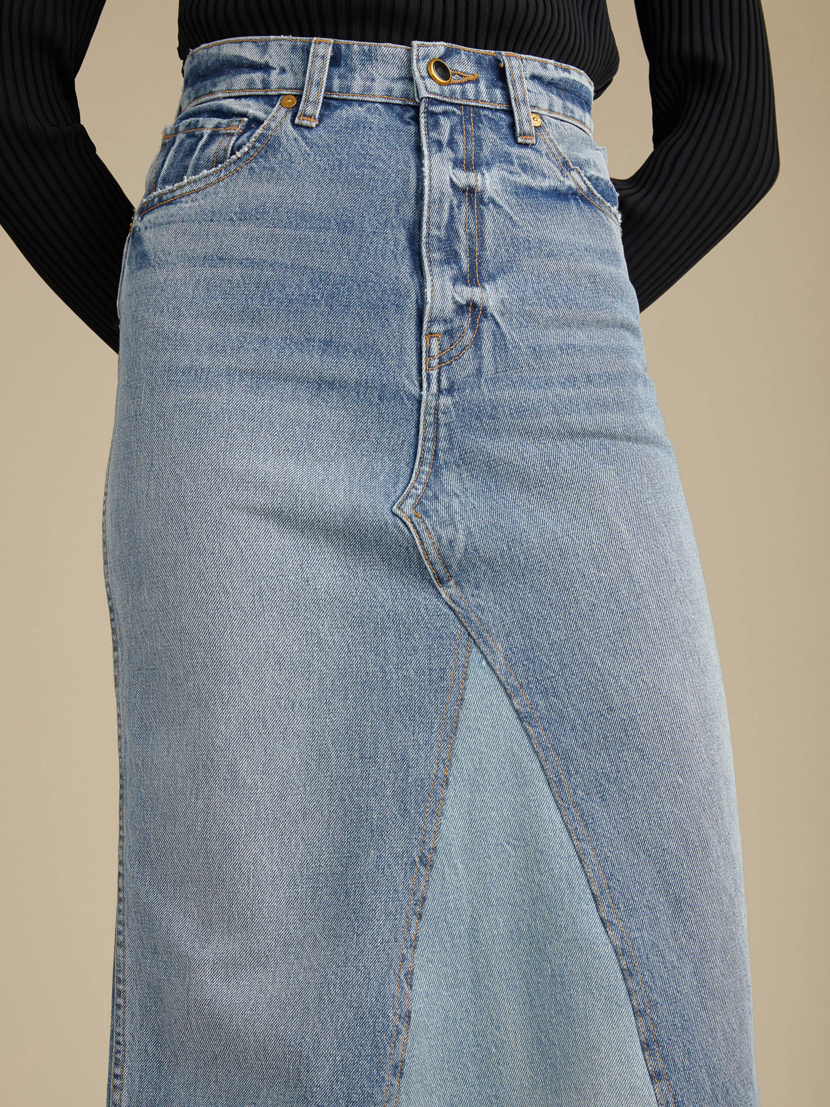 A light blue denim skirt with a lighter blue panel in the center front, presented against a neutral-toned studio backdrop.