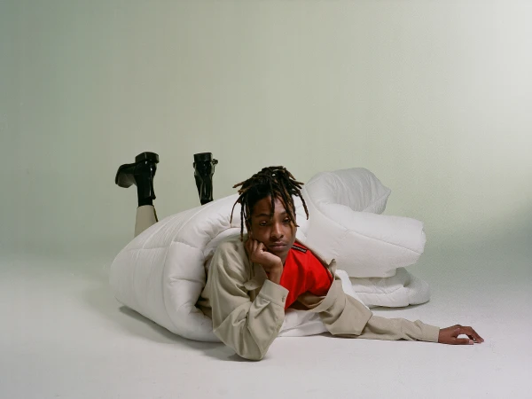 Person in an oversized white puffy comforter with black heeled boots against a light grey backdrop in a studio fashion shoot.