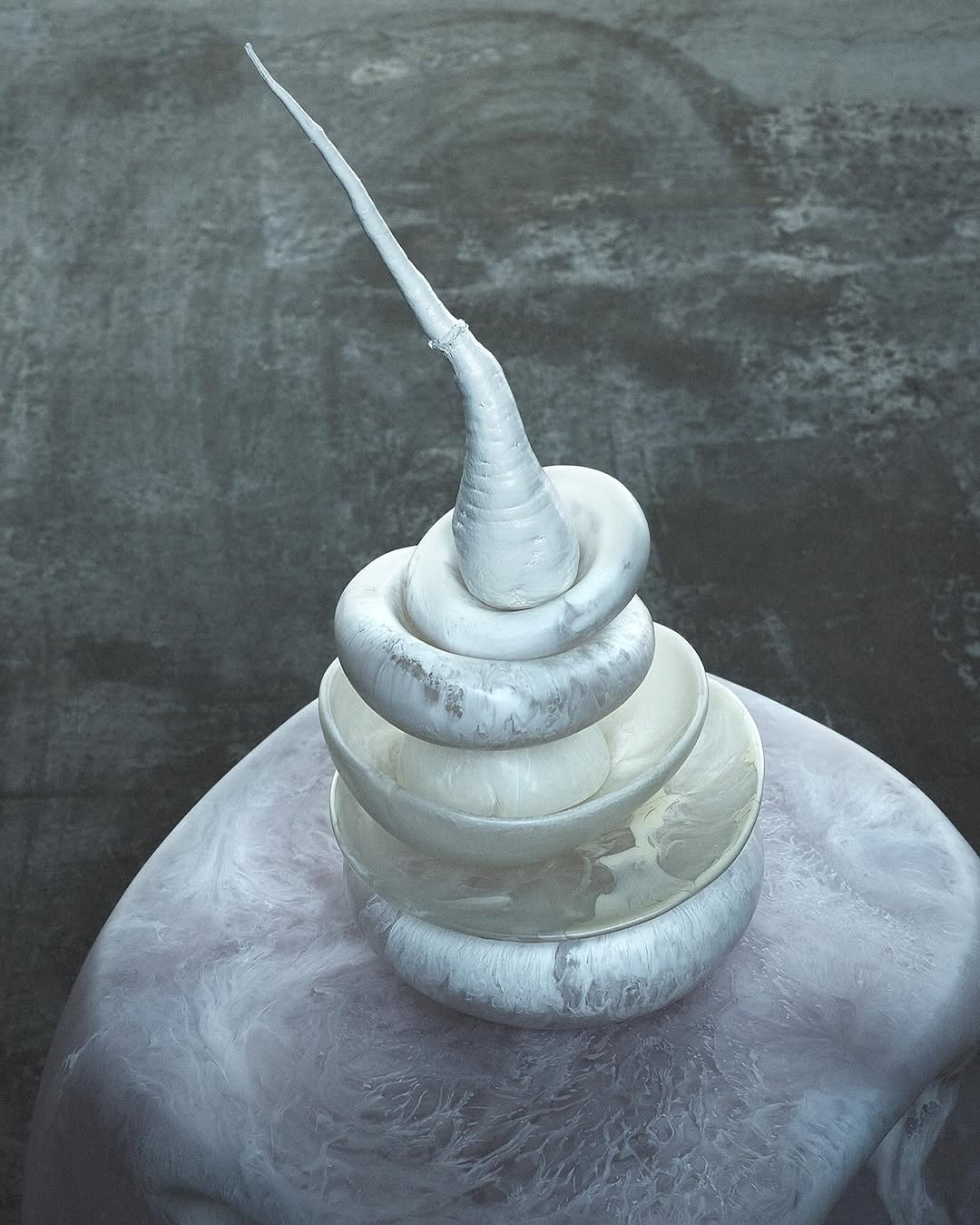 Abstract image of a stacked white sculpture composed of bowls and coils, set against a textured gray backdrop, showcasing artistic design.