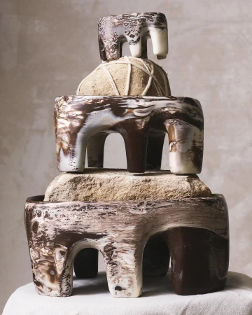 Abstract stack of three ceramic sculptures with white and brown marbling on a white cloth against a light background in studio lighting.