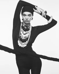 Model wearing a black cap and long-sleeved black top adorned with chunky statement necklaces and bracelets against a white background