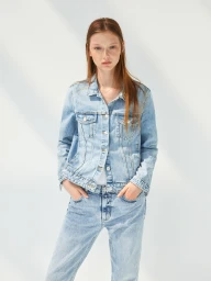 Young woman with long reddish-brown hair wearing a light blue denim jacket and matching jeans against a bright white background