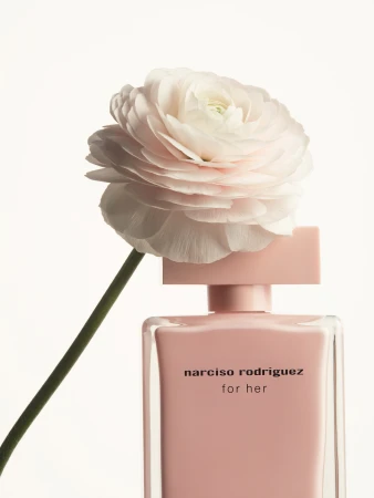 Narciso Rodriguez 'for her' perfume bottle with soft pink liquid, topped with a large pale pink ranunculus flower against a white background.