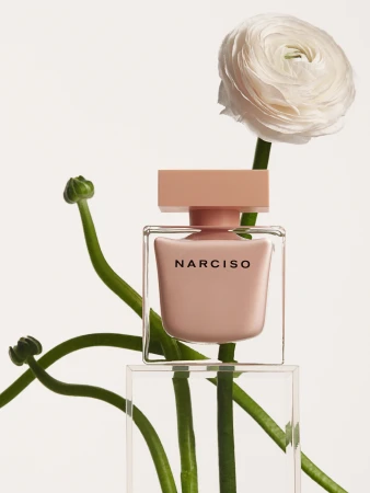 Elegant beauty shot of Narciso Rodriguez perfume bottle with ranunculus flower on bright backdrop, displaying cosmetic product beautifully.