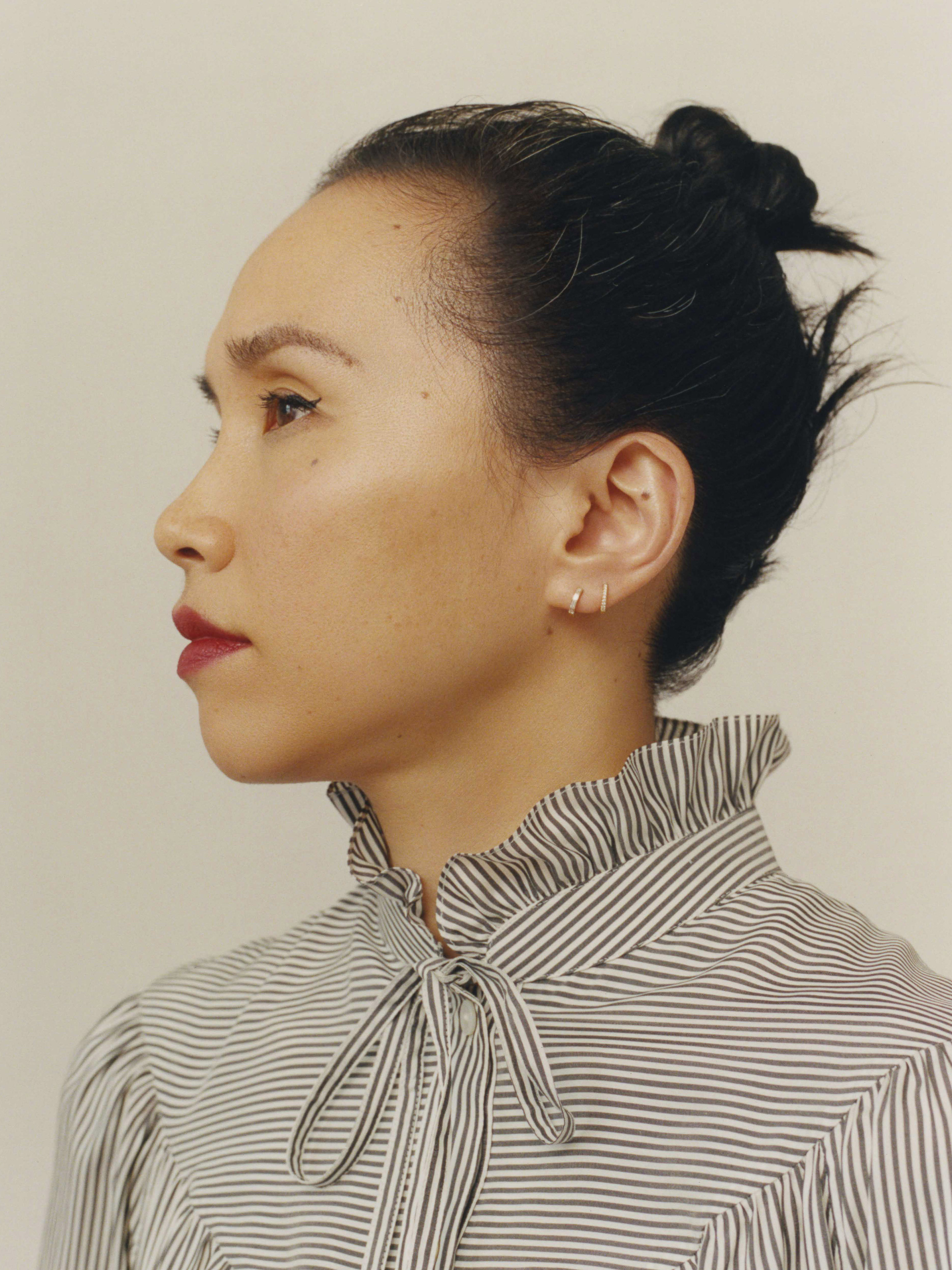 Profile shot of an adult female with dark hair in a bun, wearing a striped shirt, against a neutral background in a photo studio.