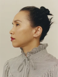 Profile portrait of an East Asian woman wearing a striped high-collar blouse with a tied bow, photographed against a neutral background.