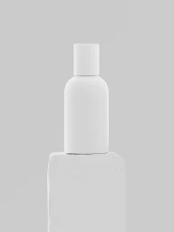 A minimalist matte white cosmetic bottle resting atop a pale rectangular stone plinth against a light grey seamless background.