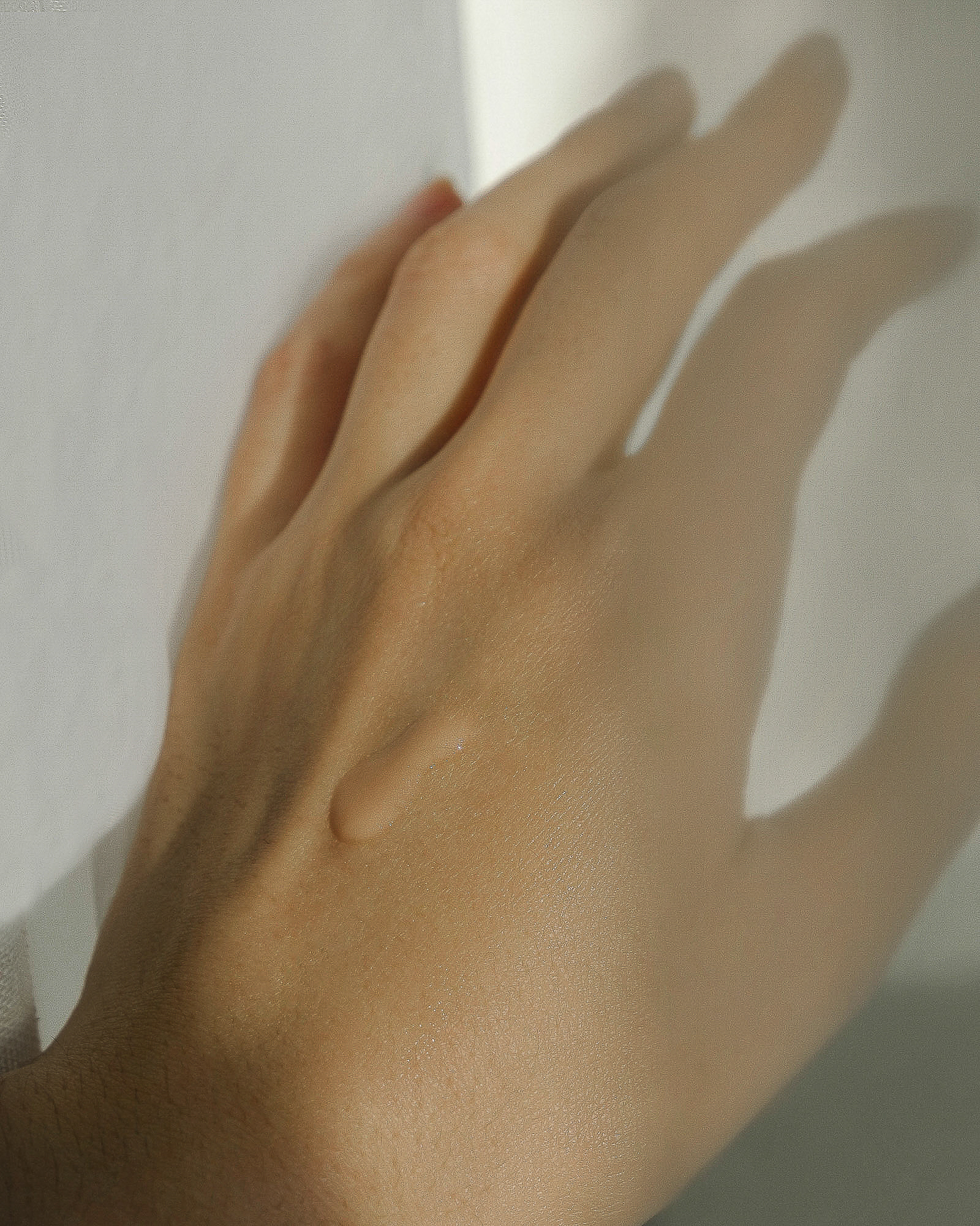 Close-up of a woman's hand with a drop of light brown lotion, bright natural lighting, and a soft, minimalist aesthetic.