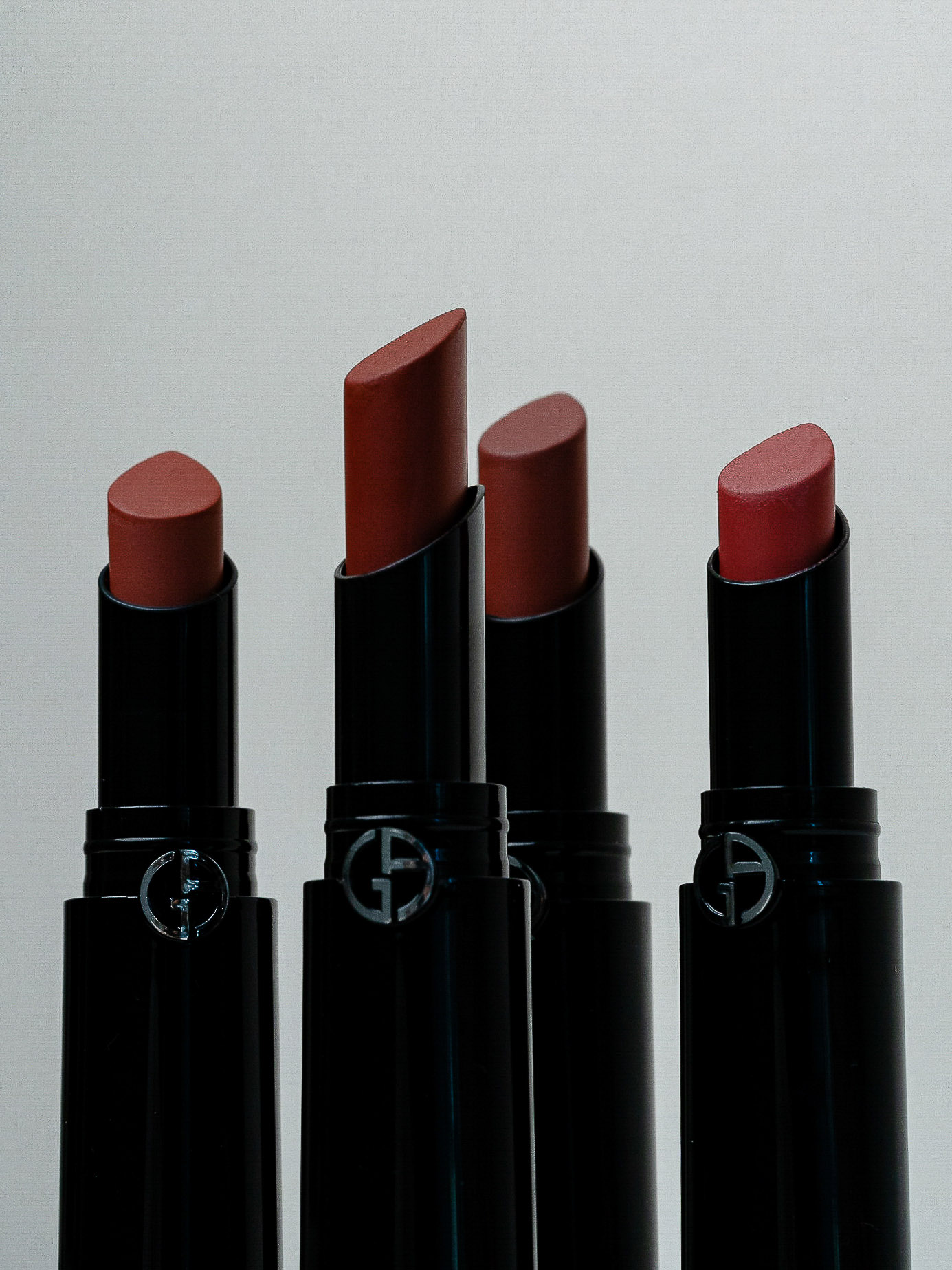 Four Giorgio Armani lipsticks in a row against a light background, showcasing different shades of color in a product shot.