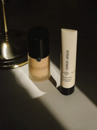 Giorgio Armani Luminous Silk foundation and primer products sit on a light surface in a dimly lit room with golden accents.