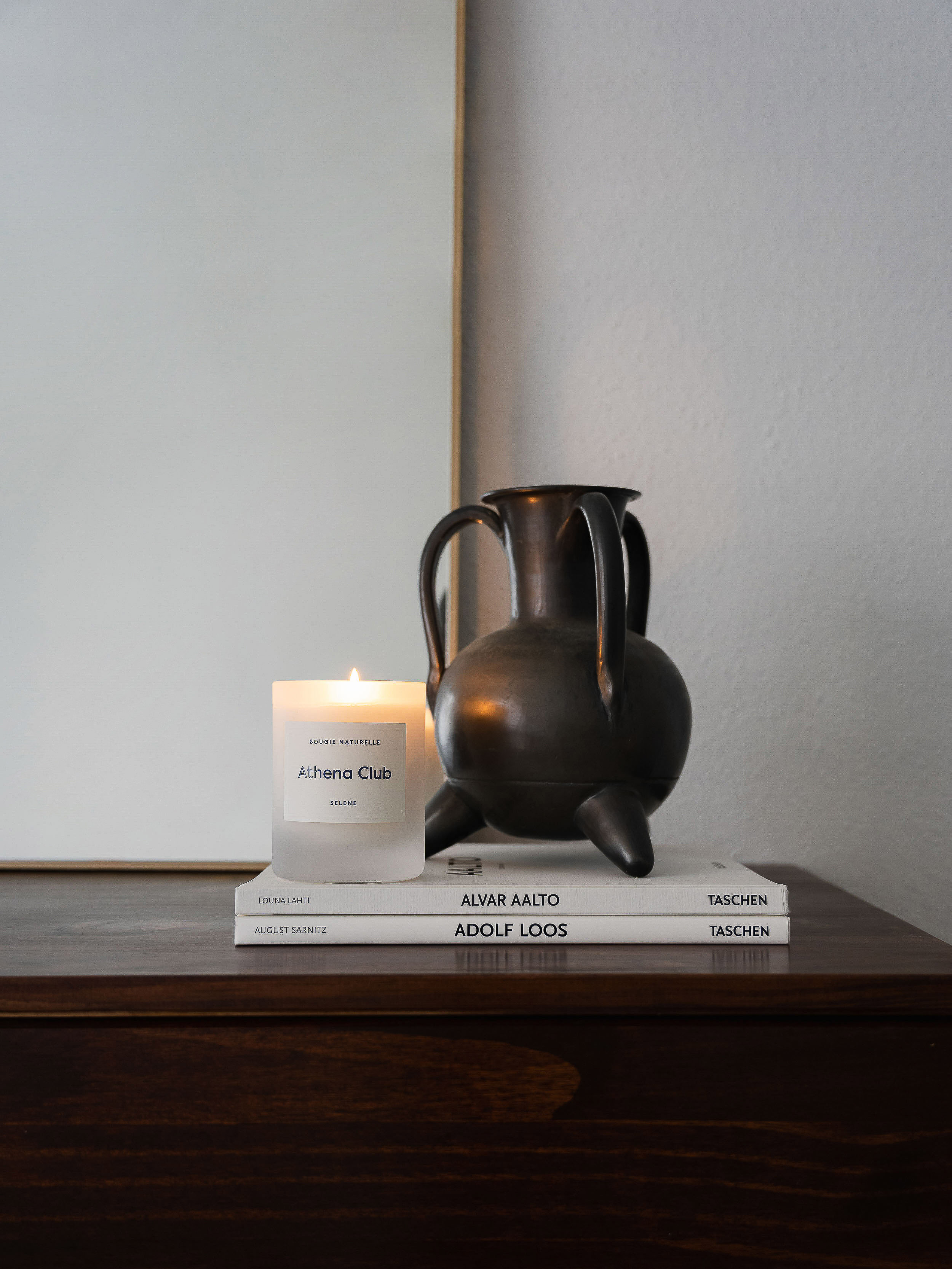 Still life of a candle, vase, and books on a dark wooden surface in an indoor setting, showcasing home decor and minimalist design.