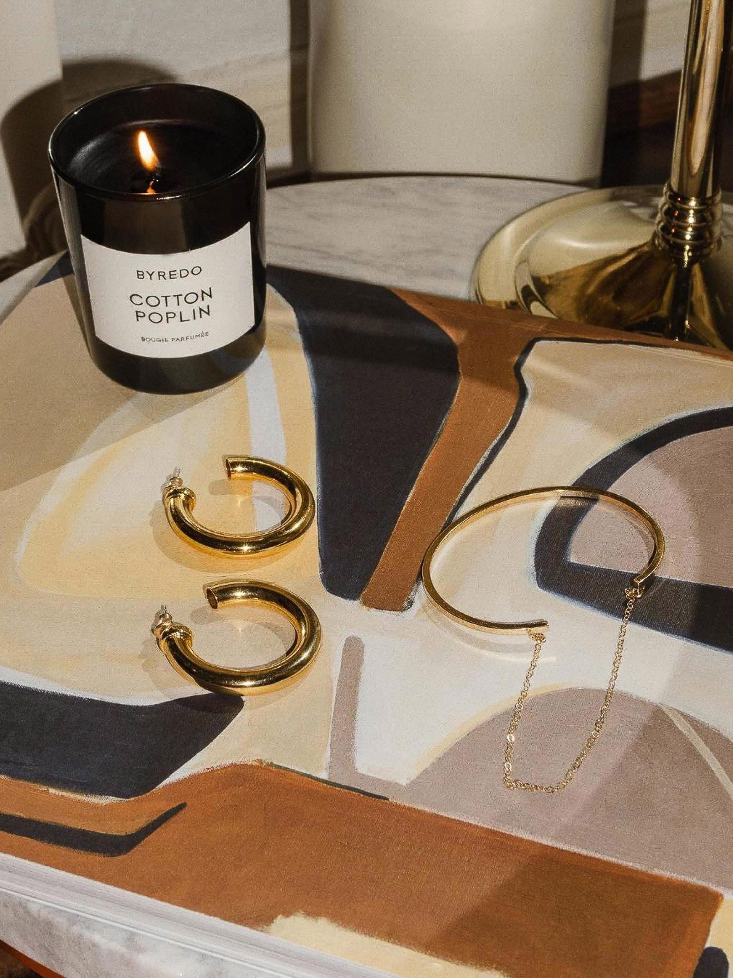 Elegant composition featuring gold jewelry, a Byredo candle, and an artful surface creates a luxurious and aesthetically pleasing scene.