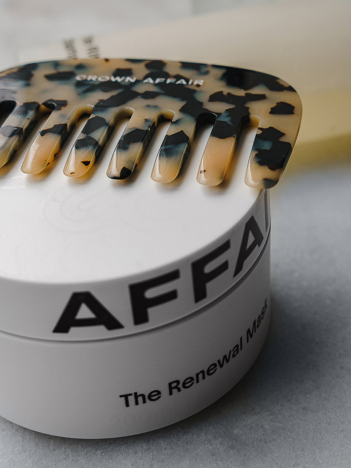 Crown Affair hair comb resting on top of a white jar labeled 'AFFAIR The Renewal Mask' in a beauty or product photography setting.