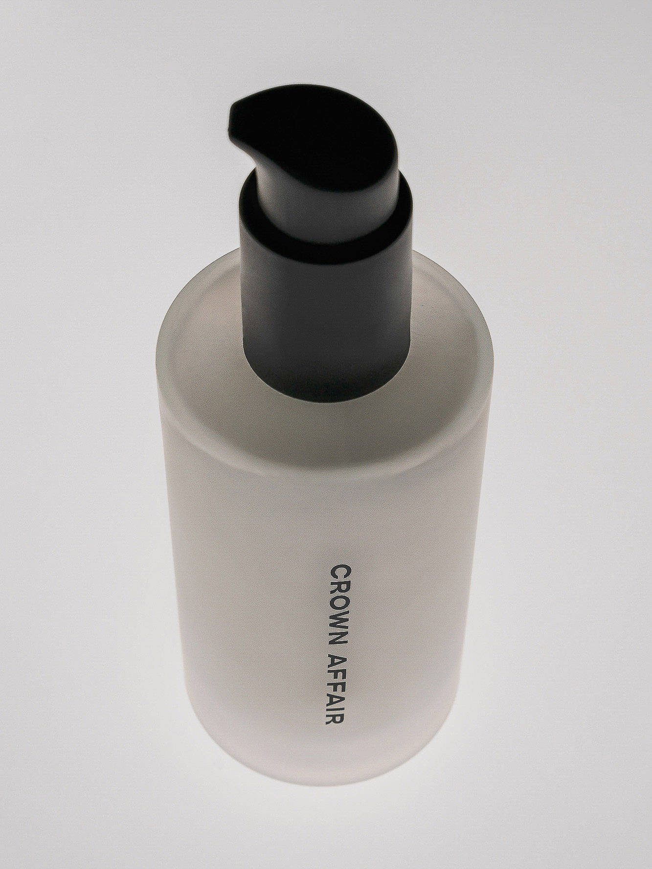 Close-up studio shot of a white bottle with a black pump dispenser, labeled 'Crown Affair', against a plain white background.