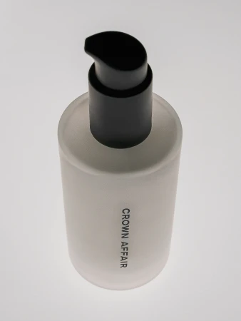 Close-up studio shot of a white bottle with a black pump dispenser, labeled 'Crown Affair', against a plain white background.