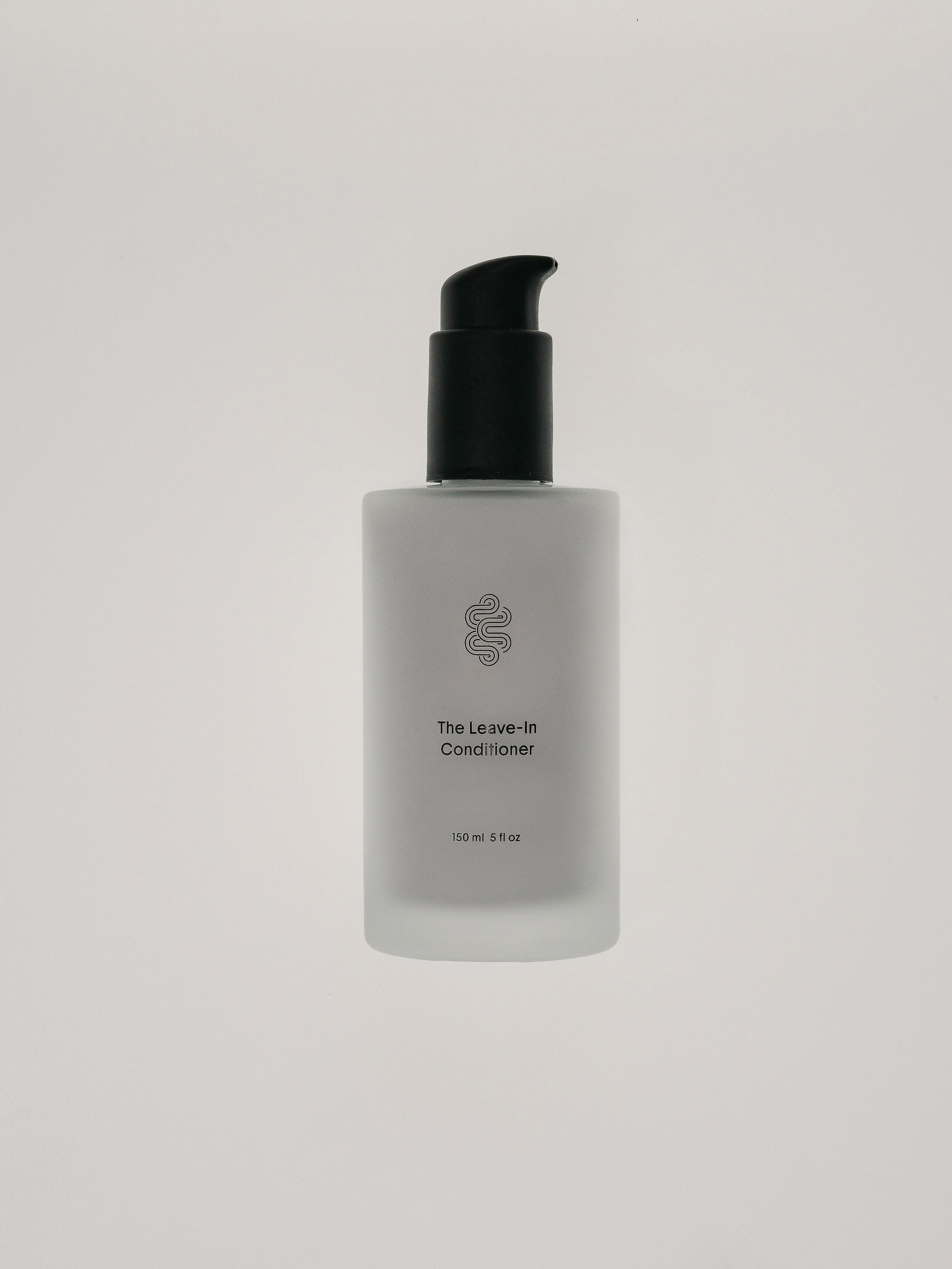 Frosted glass bottle of leave-in conditioner with a black pump, set against a plain white background, showcasing minimalistic design.
