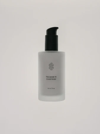 Frosted glass bottle of leave-in conditioner with a black pump, set against a plain white background, showcasing minimalistic design.