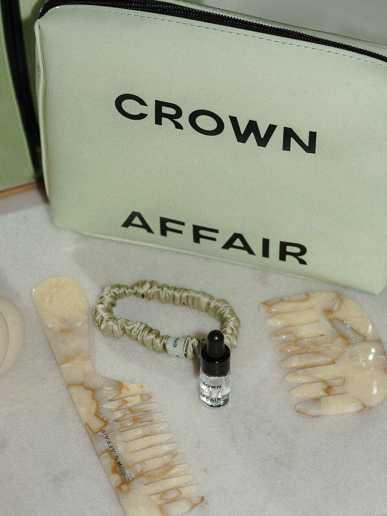 Crown Affair branded makeup bag with combs, oil and hair tie displayed against a marble background in a softly lit setting.