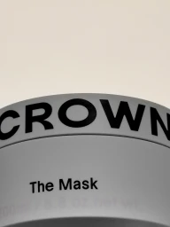 Extreme close-up of a white Crown Affair The Mask cosmetic jar showing black bold typography on the rim against a neutral background.