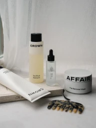 Crown Affair haircare bottles, renewal mask jar, conditioner tube, and tortoiseshell comb arranged by a sheer white curtain.