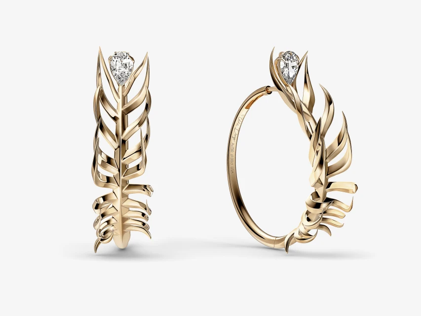A pair of sculptural gold hoop earrings featuring a leaf-like design and set with a small diamond, showcased against a white backdrop.