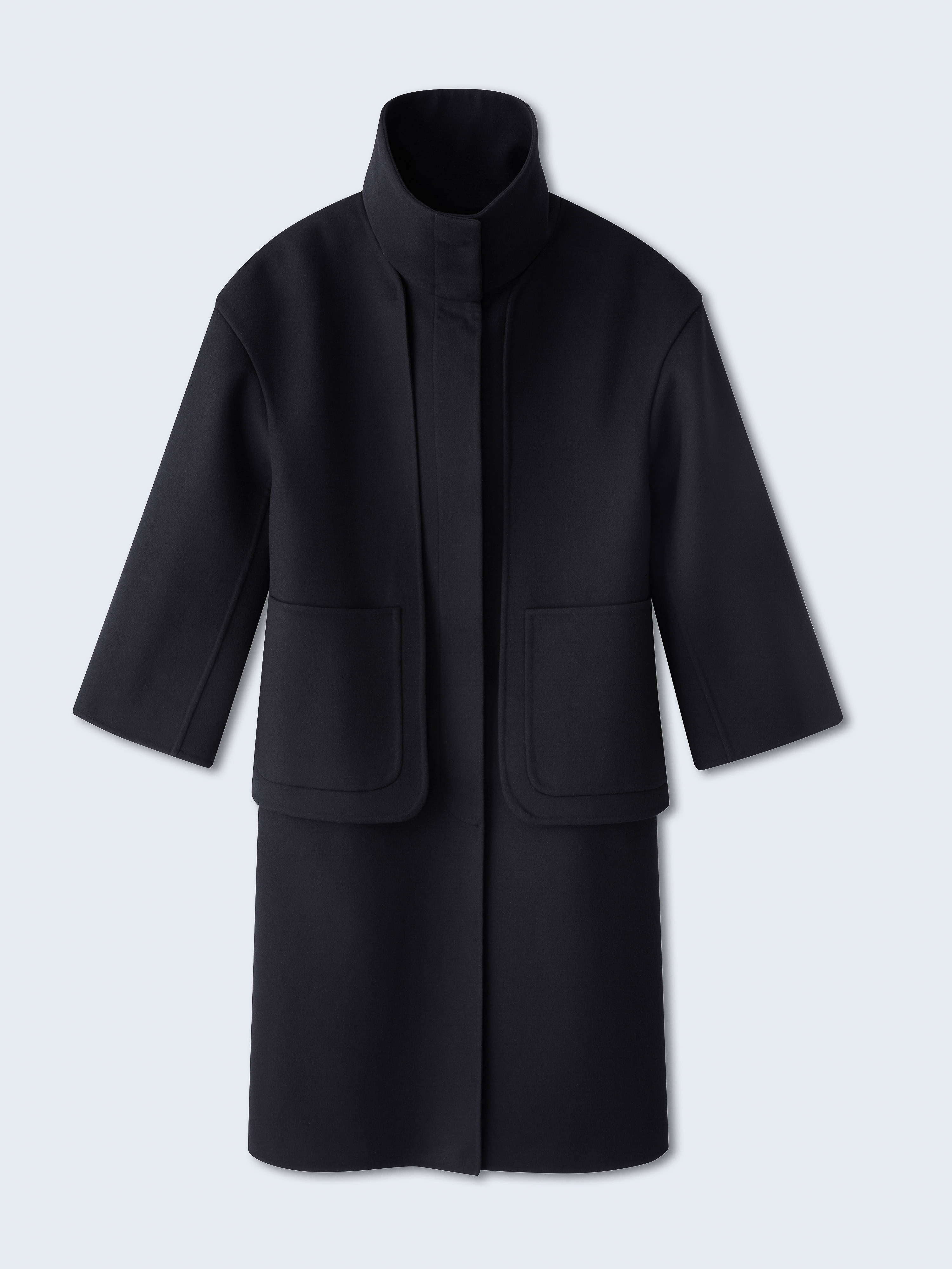 Studio shot of a black wool coat, featuring a high collar and boxy silhouette, set against a gradient blue backdrop. Minimalist fashion.
