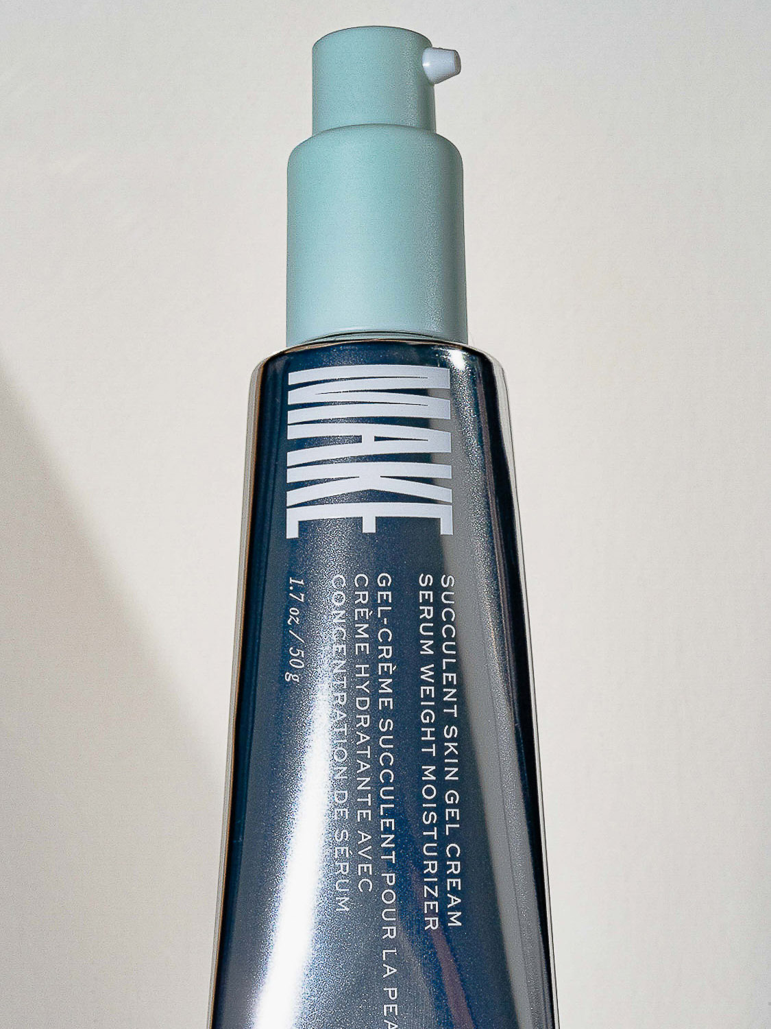Close-up of a gray bottle of Succulent Skin Gel Cream by MAKE with a light blue pump dispenser on a neutral background.