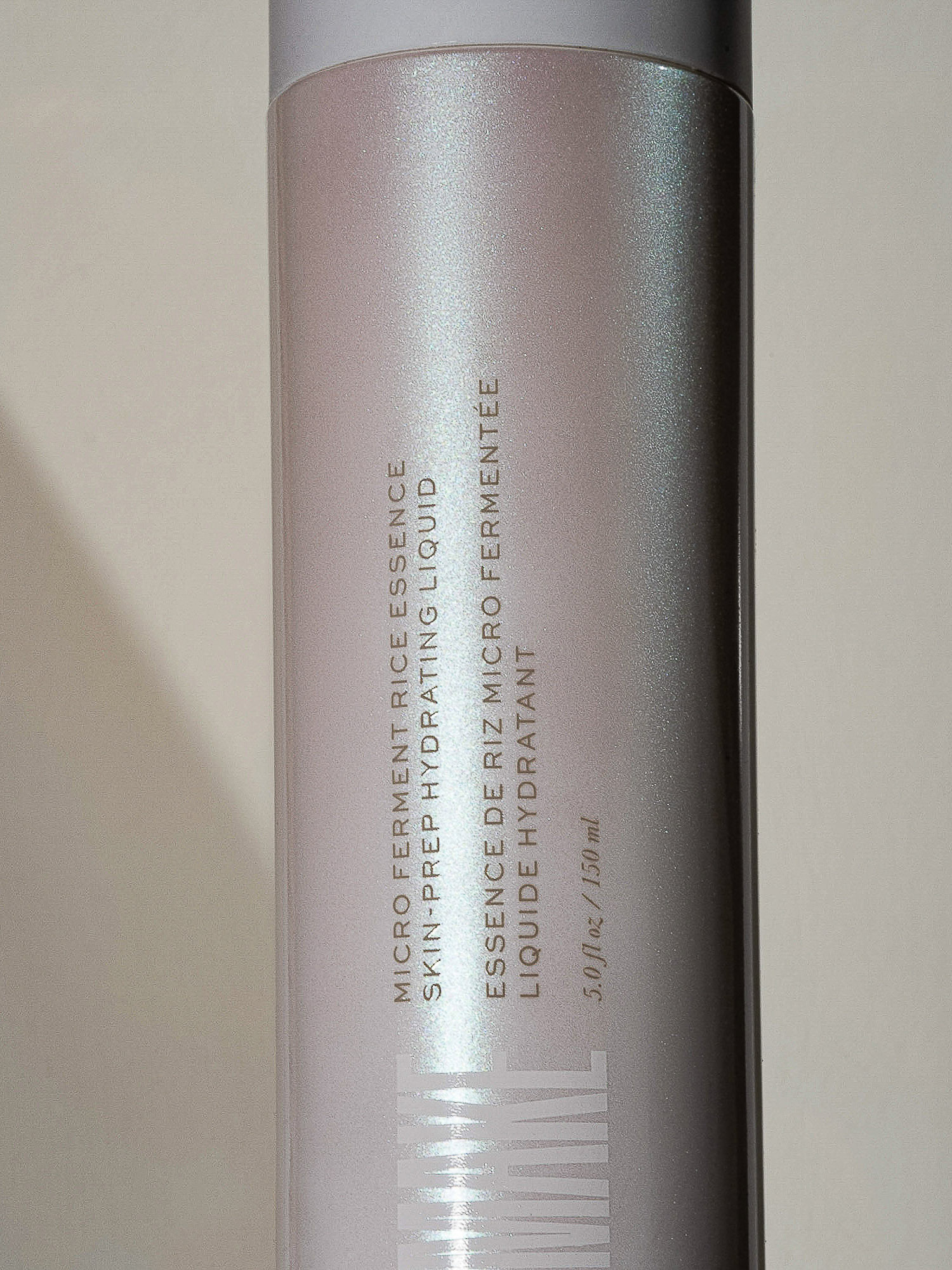 Close-up of a cylindrical white bottle of micro ferment rice essence hydrating liquid, showcasing its packaging and product information.