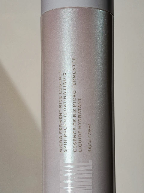Close-up of a cylindrical white bottle of micro ferment rice essence hydrating liquid, showcasing its packaging and product information.