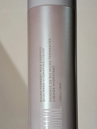 Close-up of a cylindrical white bottle of micro ferment rice essence hydrating liquid, showcasing its packaging and product information.
