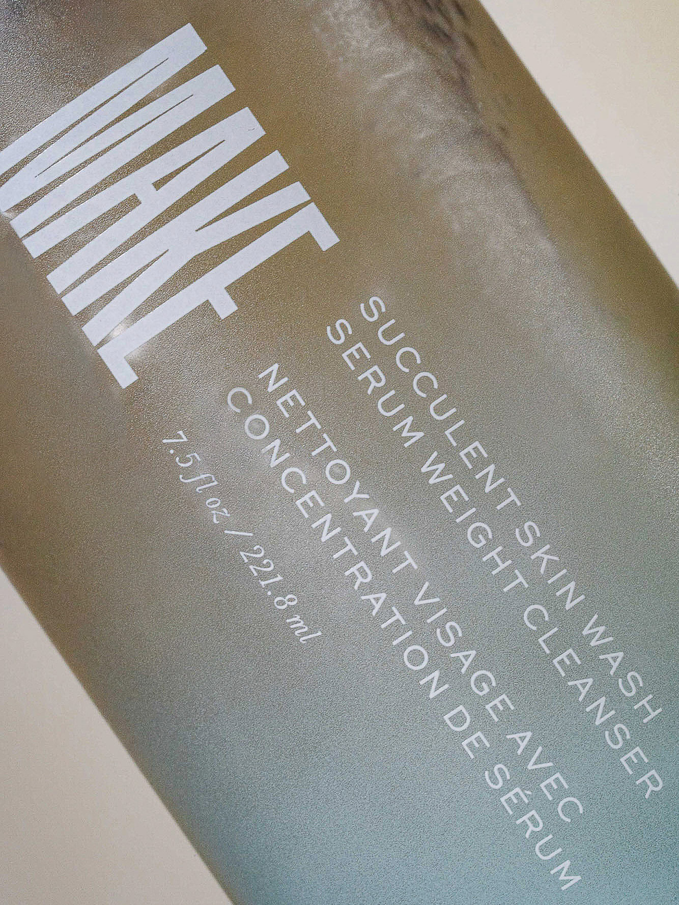 Close-up of a bottle of MAKE Succulent Skin Wash Serum Weight Cleanser with white sans-serif text on a metallic gradient background.