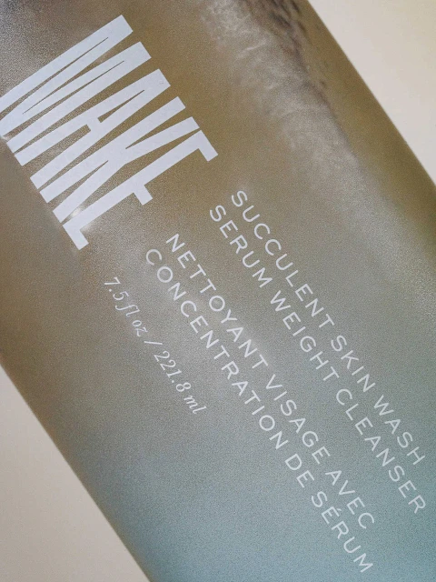 Close-up of a bottle of MAKE Succulent Skin Wash Serum Weight Cleanser with white sans-serif text on a metallic gradient background.