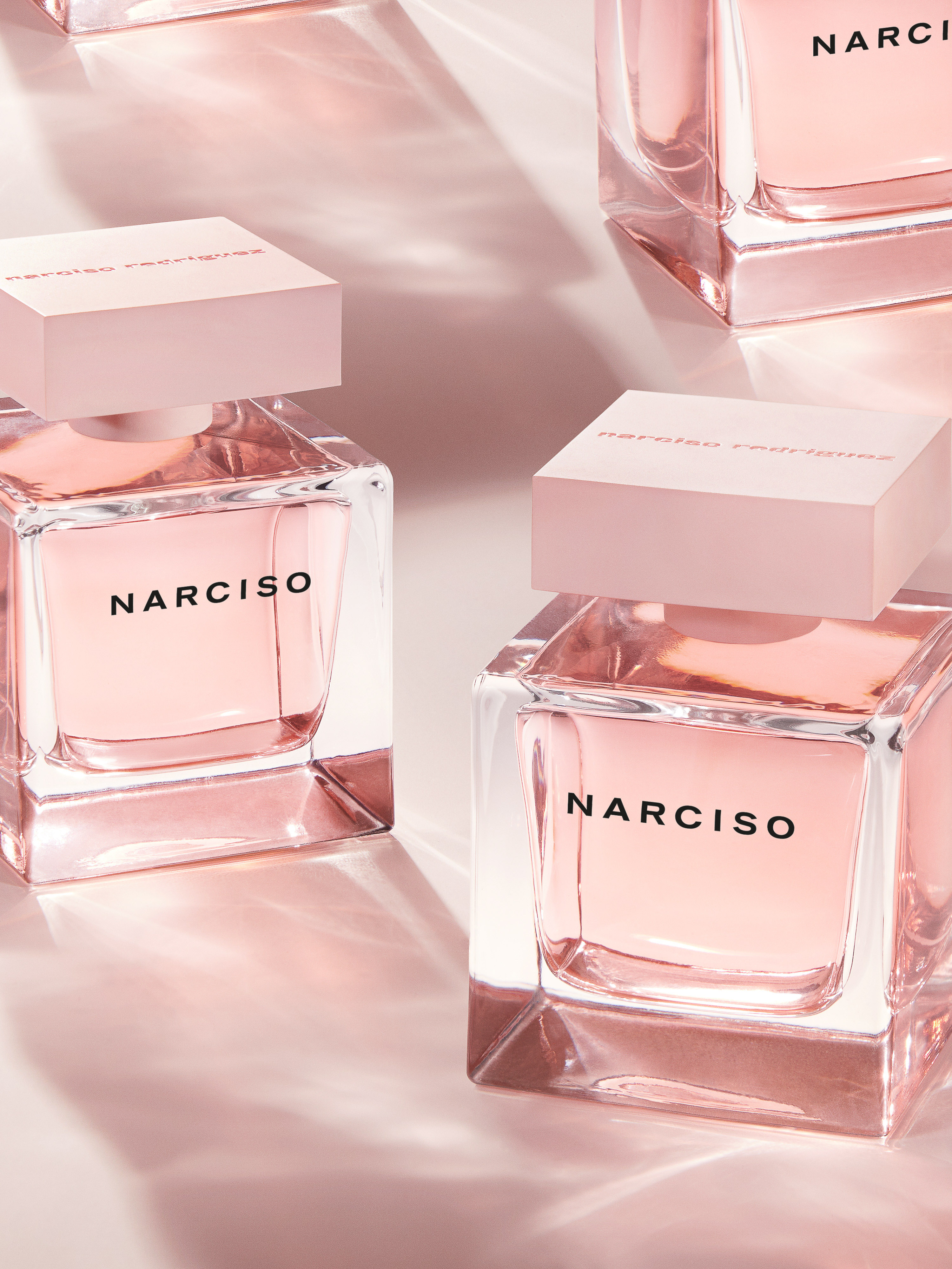 Multiple Narciso Rodriguez perfume bottles with pink lids and clear glass on a pink backdrop, in a beauty and product photography style.