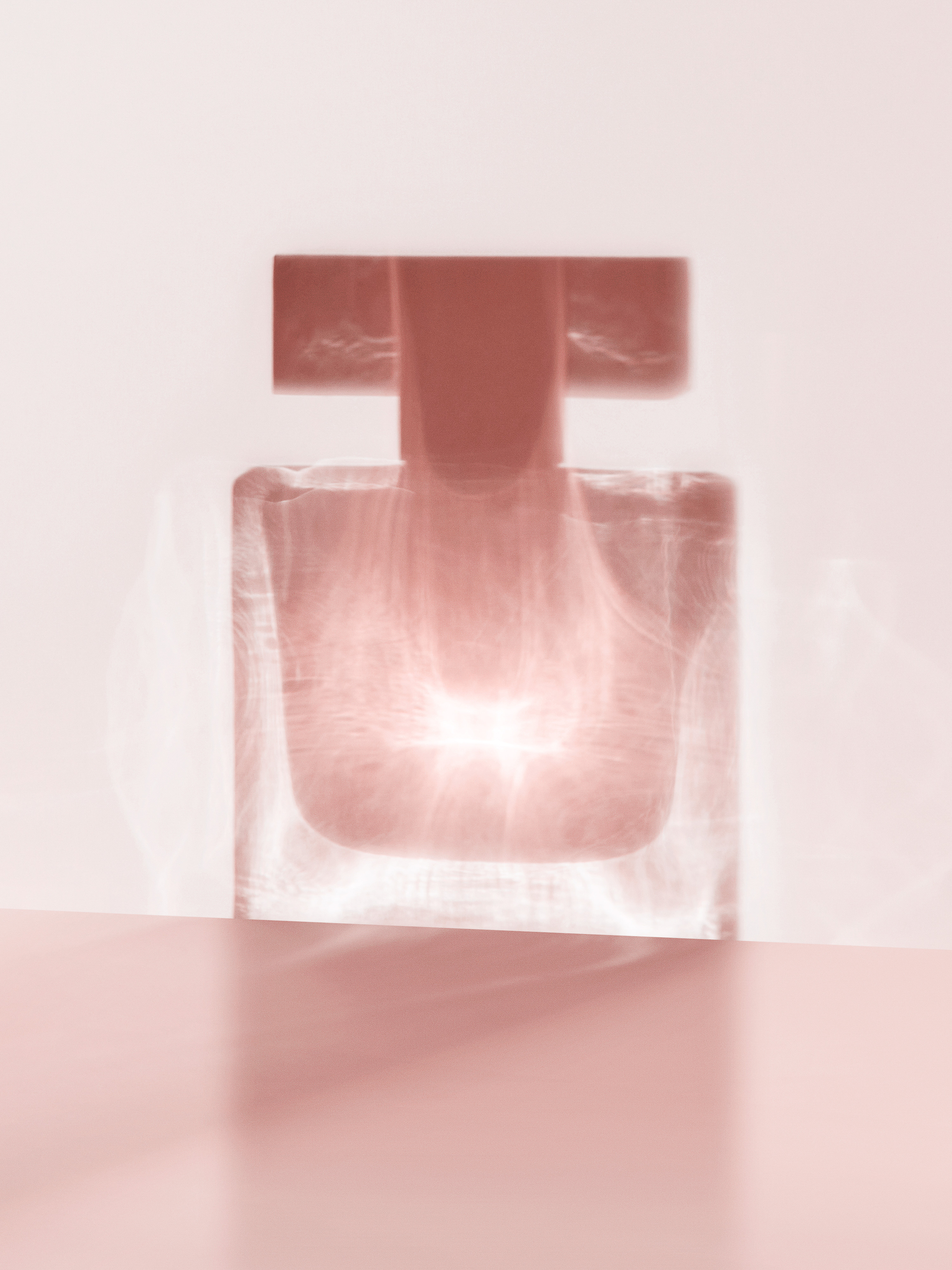 Still life of a transparent glass perfume bottle on a pink surface, capturing diffused light and soft shadows.