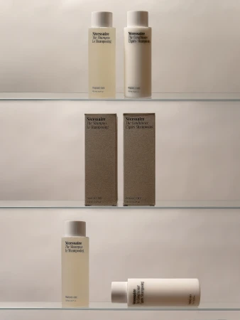Minimalist beauty product display featuring a collection of Nécessaire shampoo and conditioner bottles and boxes on clear glass shelves.