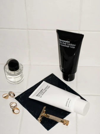 Cosmetic product arrangement featuring a black tube, white bottle, clear bottle, and safety razor on a black tile surface.