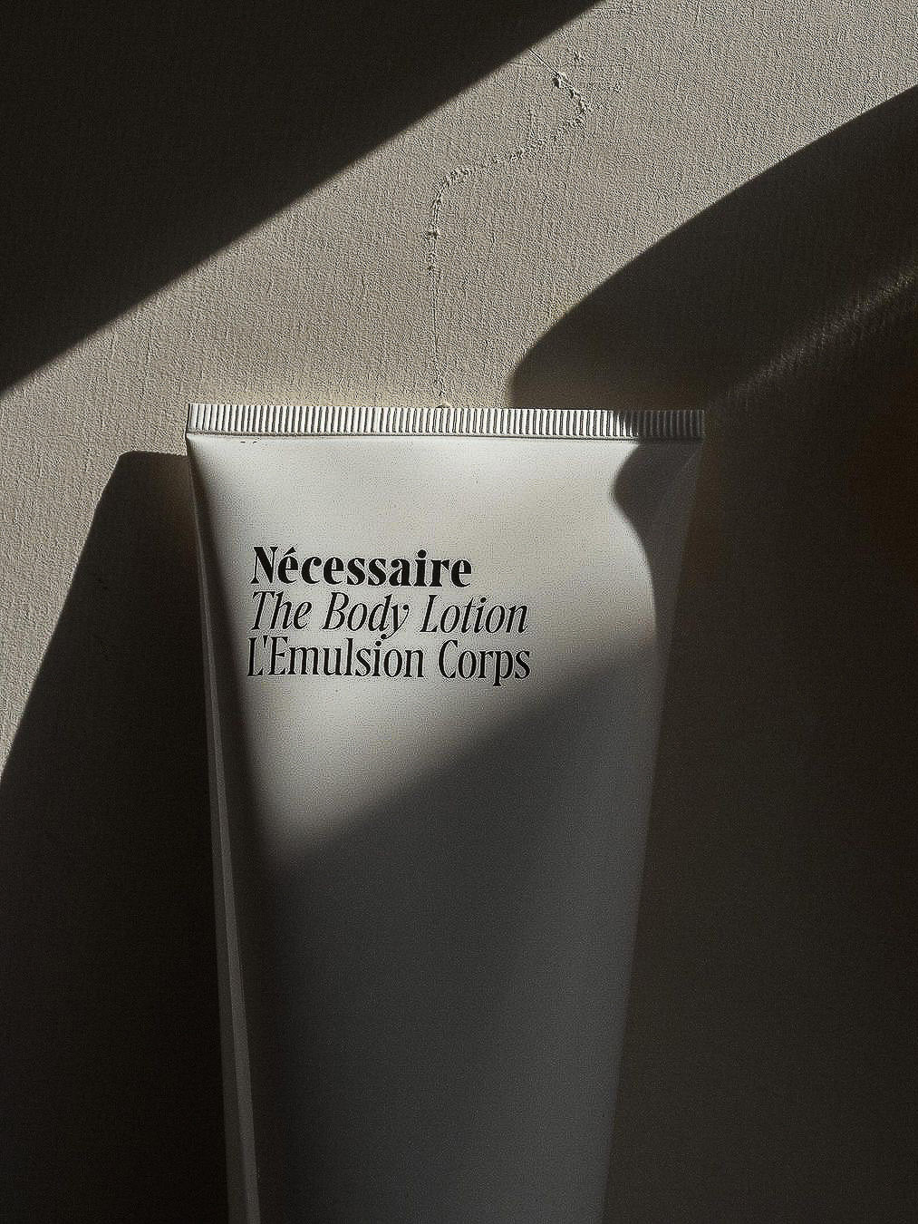 Close-up of a white tube of Nécessaire The Body Lotion L'Emulsion Corps against a neutral background with strong shadows.