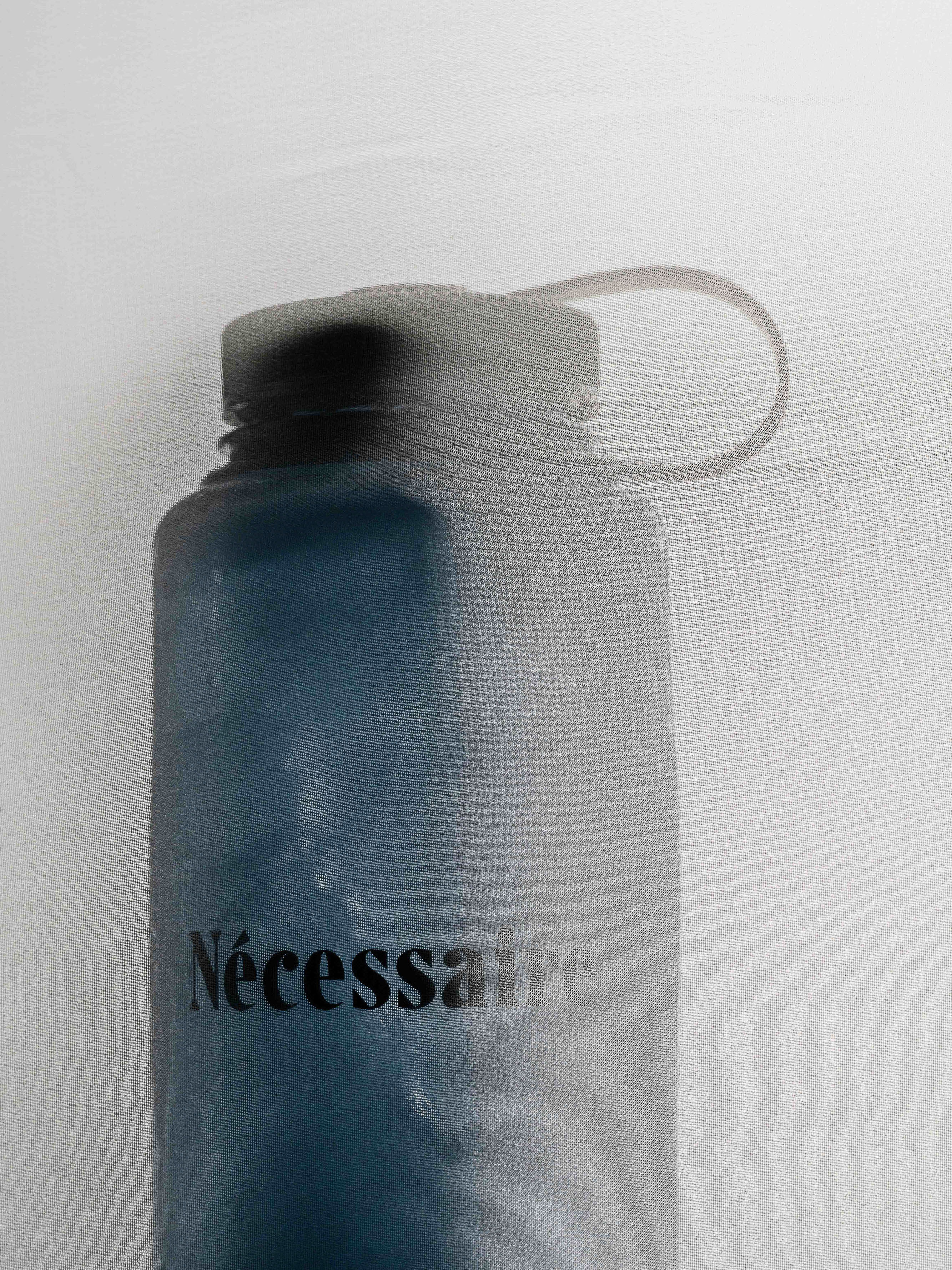 Close-up of a blue Nalgene water bottle with a black lid and the text 'Nécessaire' printed on the side, set against a white background.