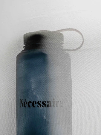 Close-up of a blue Nalgene water bottle with a black lid and the text 'Nécessaire' printed on the side, set against a white background.