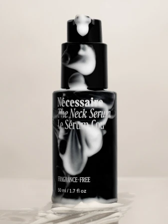 Necessaire The Neck Serum in a black bottle with white foam on a neutral background, product shot for beauty and personal care.