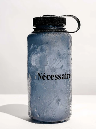 Blue water bottle filled with ice and condensation on a white surface, featuring the word "Nécessaire" in black text.