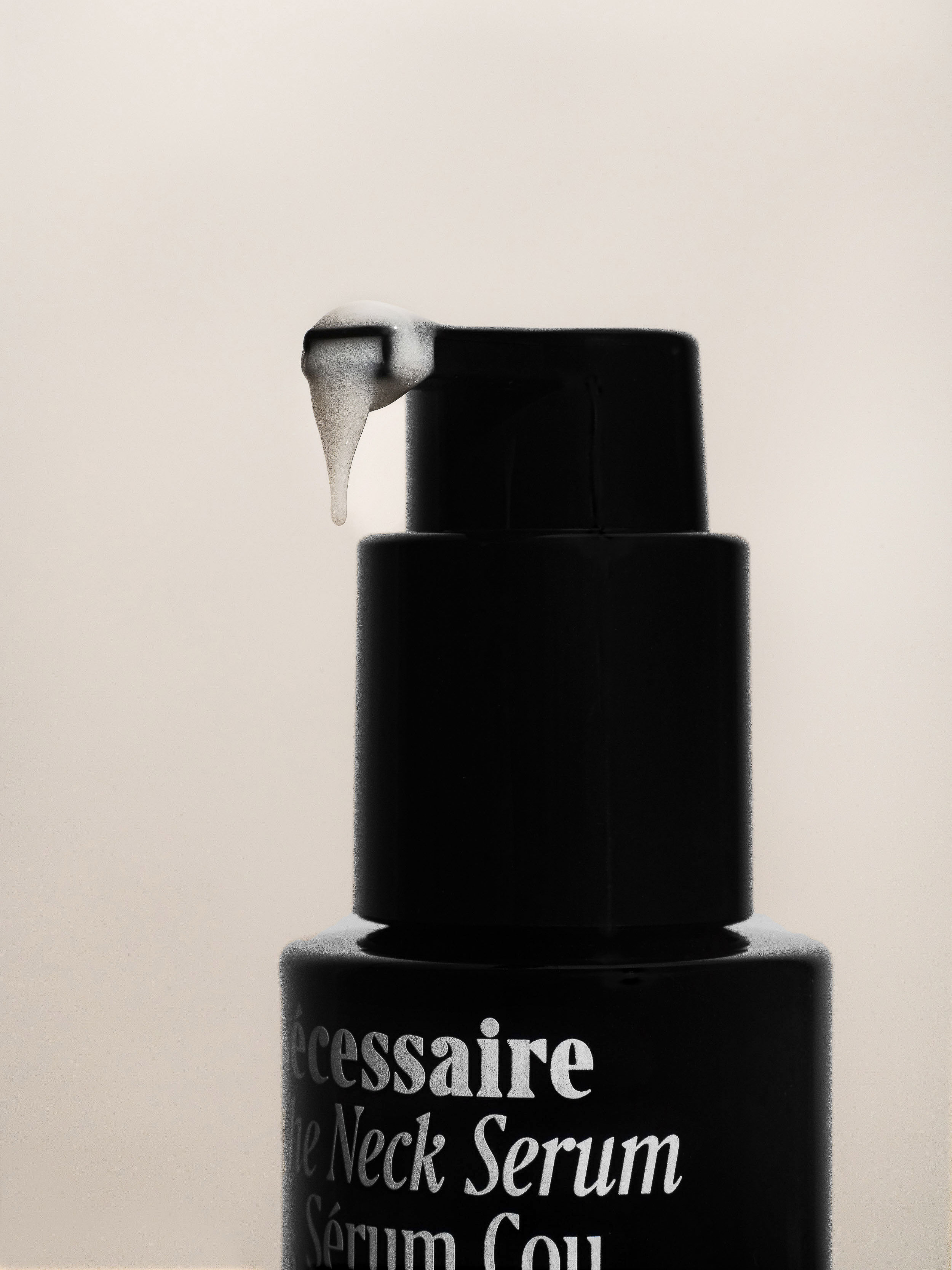 Close-up of Necessaire The Neck Serum bottle with white serum droplet against a soft, neutral background in a beauty context.