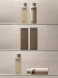 Nécessaire shampoo and conditioner bottles and boxes arranged neatly on three glass shelves against a neutral background.