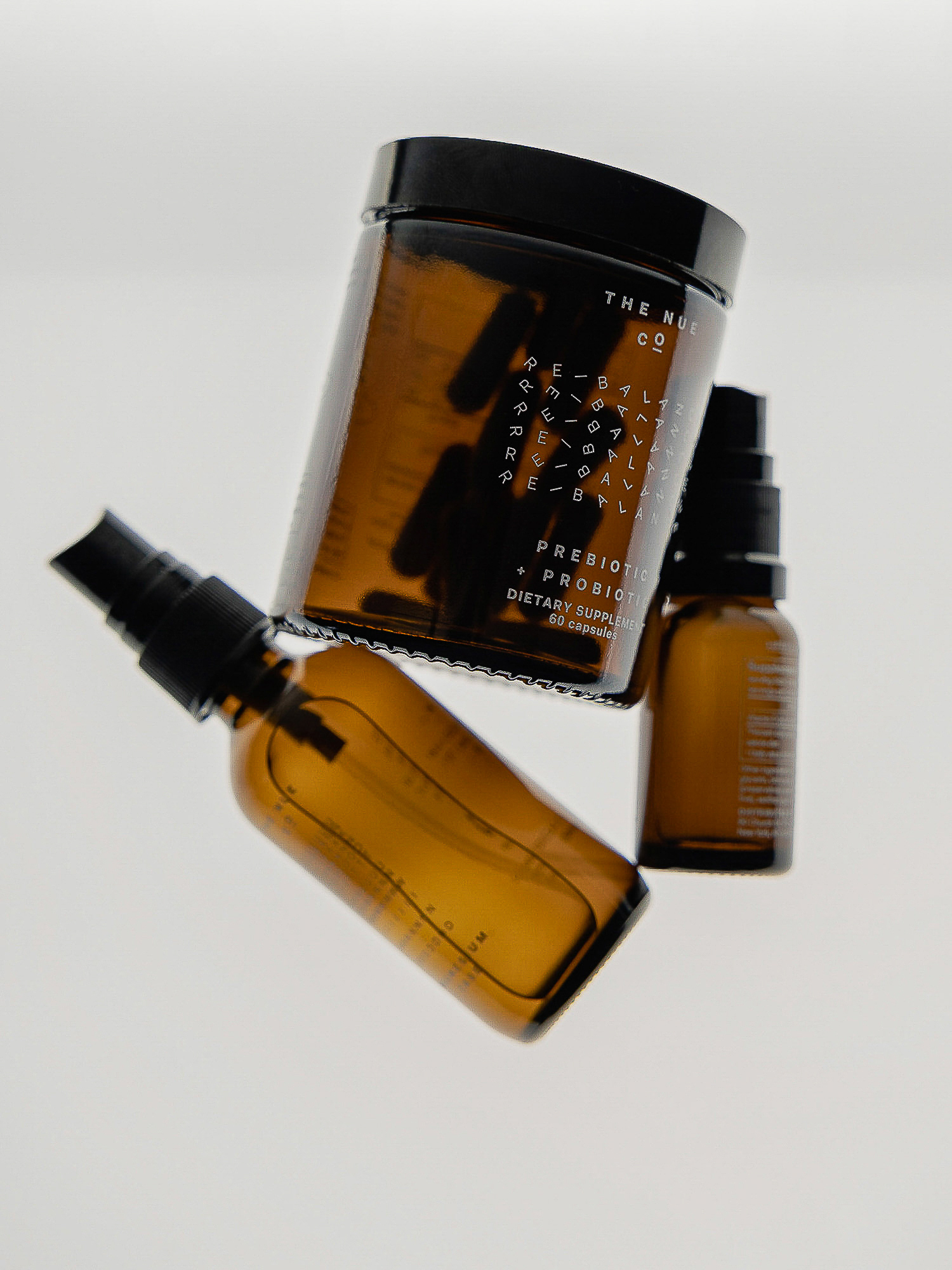 An eye-level shot features three amber glass bottles against a white backdrop, including a spray bottle and a jar with capsules inside.