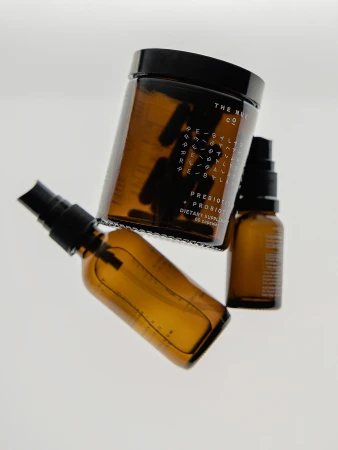 An eye-level shot features three amber glass bottles against a white backdrop, including a spray bottle and a jar with capsules inside.